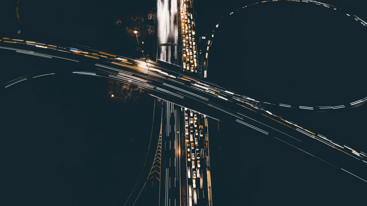 Top-down highway interchange with crossing light trails, symbolizing coupling, traffic pressure, and multi-path sequencing.