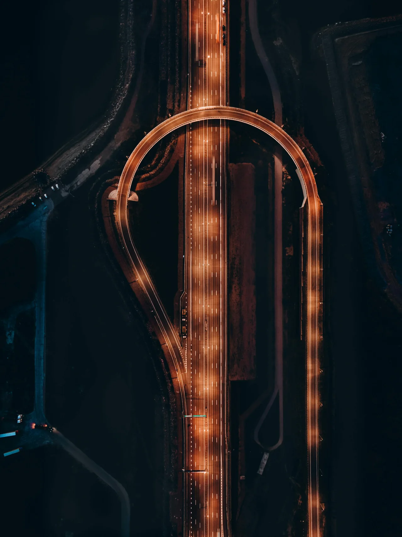 Aerial night interchange with a single glowing loop, expressing routing complexity, speed, and controlled flow under constraint.