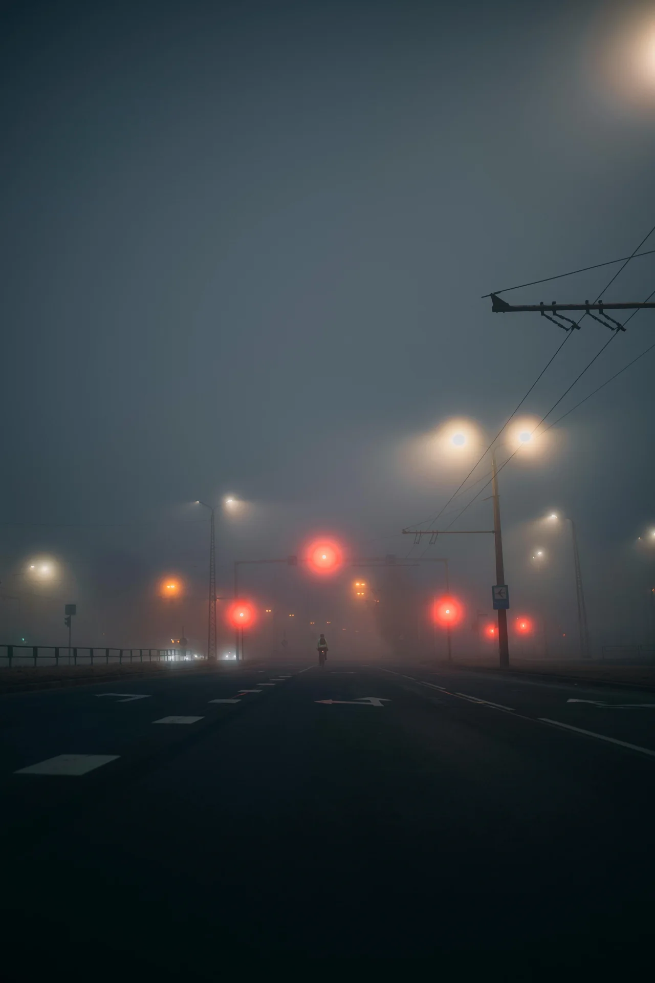 Fog-bound urban street with isolated signal lights, evoking uncertainty, sparse visibility, and delayed response windows.